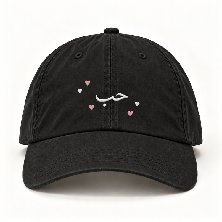 Black cap with white Arabic lettering and pink and white hearts